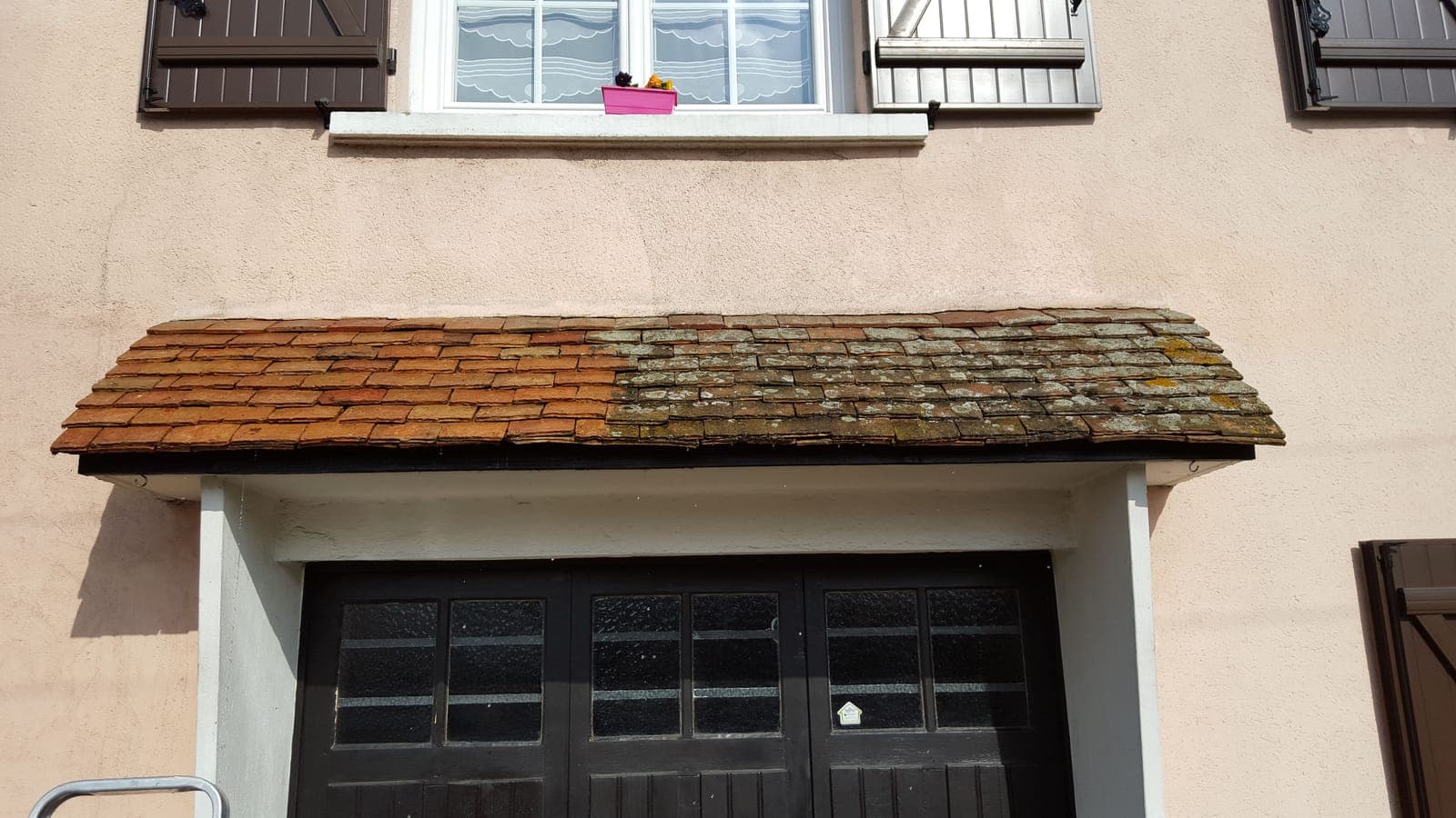 Auvent en tuiles au-dessus d'une porte de garage, moitié moussue et moitié nettoyée