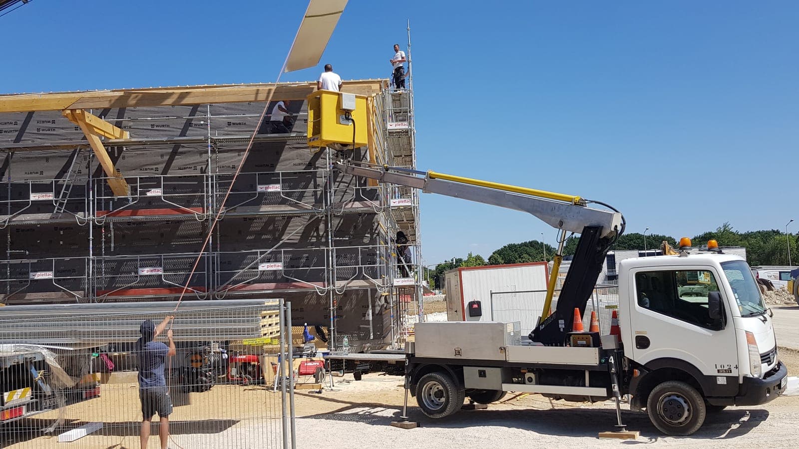 Grand bâtiment à ossature bois sous échafaudage, nacelle et camion au pied