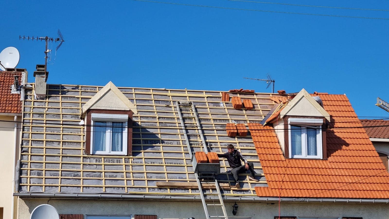 Maison à deux lucarnes, versant couvert de tuiles neuves orange à côté du versant encore sur liteaux
